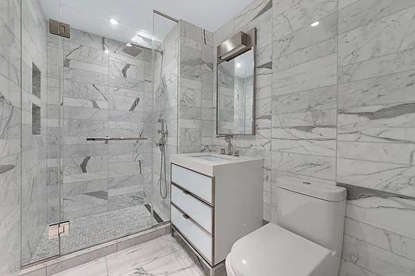 135 W 52nd St Unit 8D, New York Manhattan, NY 10019 - full bathroom with toilet, marble finish floors, vanity, a marble finish shower, and tile walls