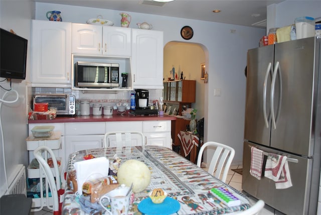 4026 208th St, Bayside, NY 11361 - kitchen with stainless steel appliances, white cabinetry, arched walkways, decorative backsplash, and tile patterned flooring