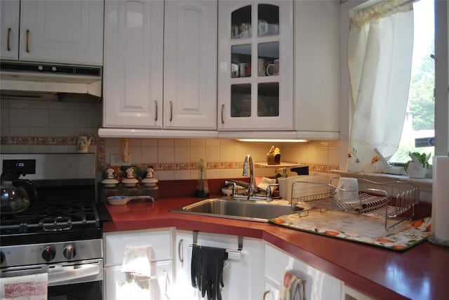 4026 208th St, Bayside, NY 11361 - kitchen featuring stainless steel gas stove, under cabinet range hood, white cabinetry, decorative backsplash, and glass insert cabinets