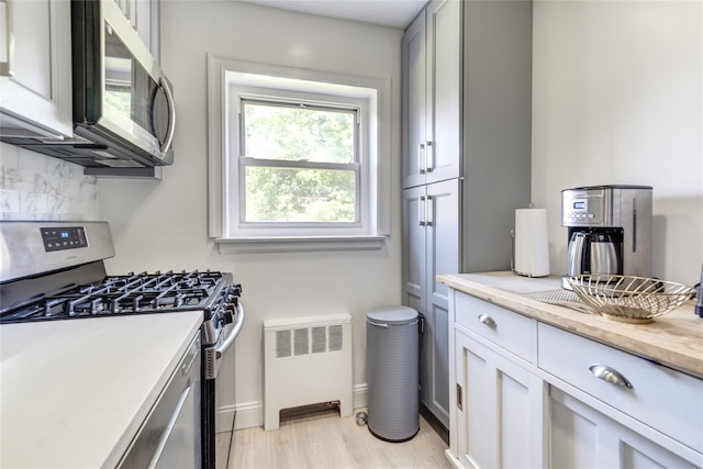 221 Middle Neck Rd Unit M-4, Great Neck, NY 11021 - kitchen with appliances with stainless steel finishes, radiator heating unit, backsplash, light wood-style floors, and light stone countertops