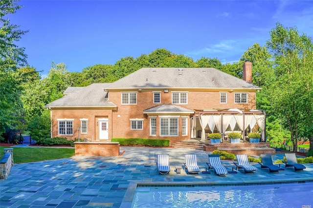 9 Stream Ct, Great Neck, NY 11024 - rear view of house with a patio area, a chimney, brick siding, an outdoor pool, and view of wooded area