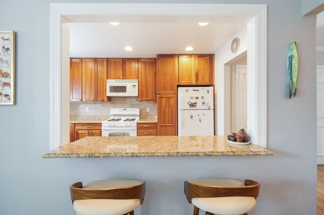 131-2 S Highland Ave Unit A3, Ossining, NY 10562 - kitchen featuring white appliances, brown cabinets, a breakfast bar area, light stone counters, and a peninsula