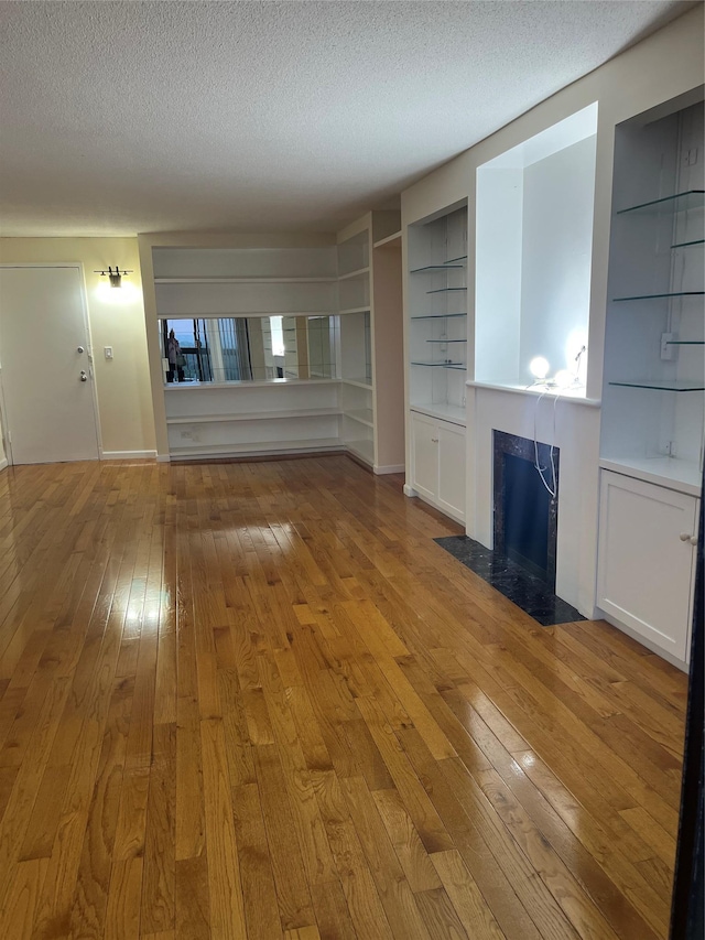 2 Bay Club Dr Unit 16N, Bayside, NY 11360 - unfurnished living room featuring light wood-type flooring, a textured ceiling, a fireplace with flush hearth, and built in shelves