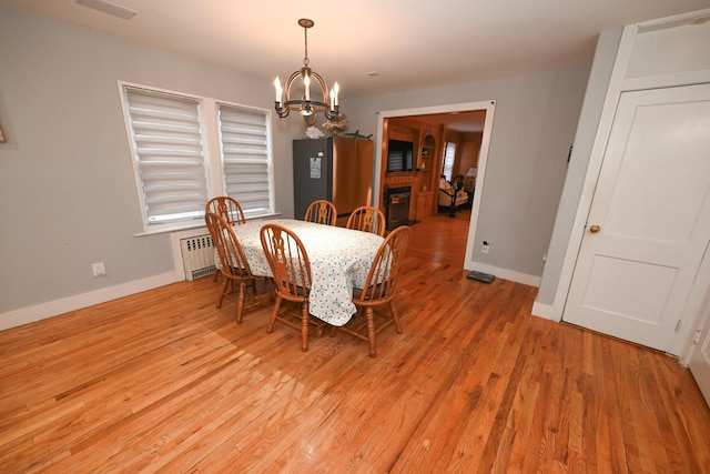 165 Page Rd, Valley Stream, NY 11581 - dining area featuring radiator heating unit, a chandelier, light wood-style flooring, and a glass covered fireplace
