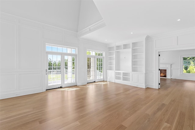 44 Club Ln, Remsenburg, NY 11960 - unfurnished living room featuring a decorative wall, built in features, light wood-style floors, a warm lit fireplace, and crown molding