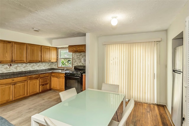 18 Hilliard Ave, Central Islip, NY 11722 - kitchen featuring black range with gas cooktop, a sink, brown cabinets, a textured ceiling, and light wood finished floors