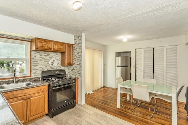18 Hilliard Ave, Central Islip, NY 11722 - kitchen featuring black gas range oven, freestanding refrigerator, a sink, light wood-type flooring, and brown cabinetry