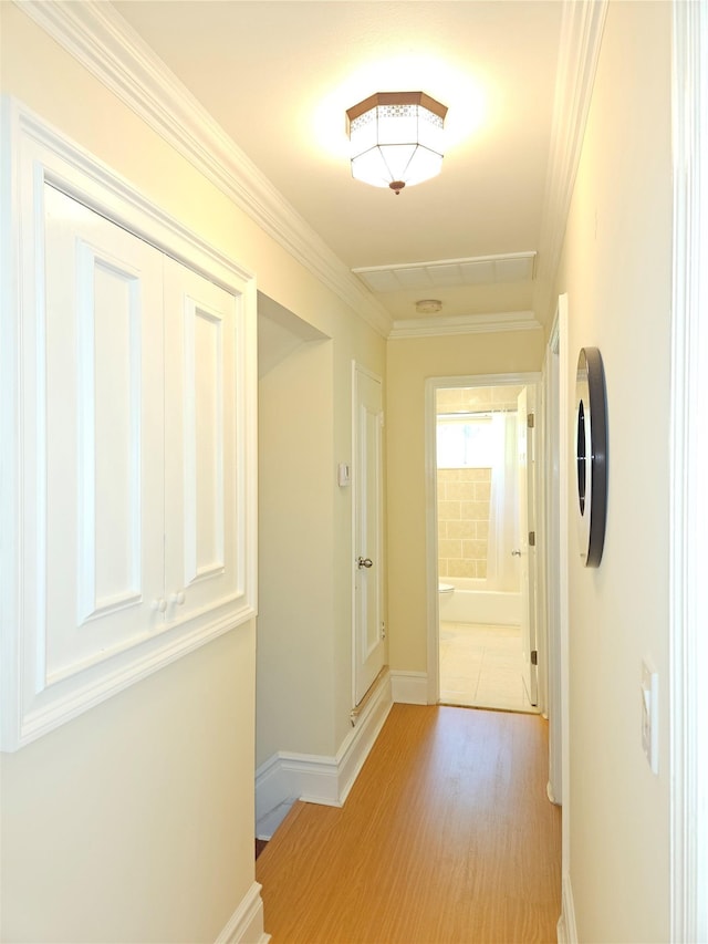 hall featuring baseboards, crown molding, and light wood-style flooring