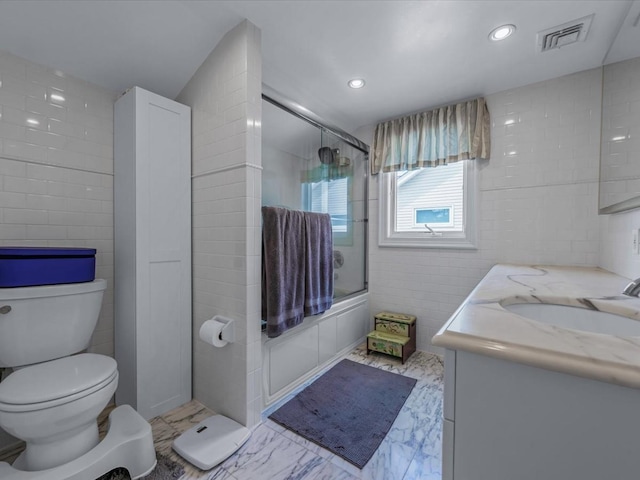 18 Ashland Ave, New Hyde Park, NY 11040 - bathroom with toilet, tile walls, vanity, marble look tiles, and bath / shower combo with glass door