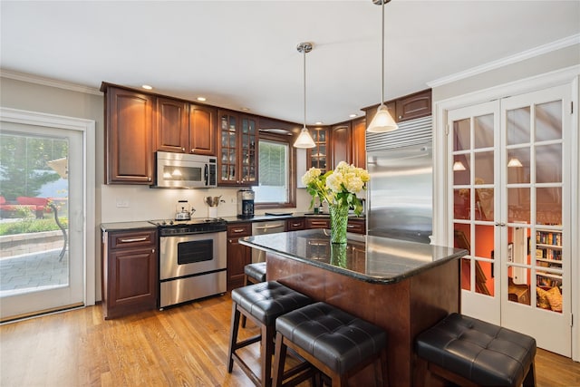 4 Valley Rd, Syosset, NY 11791 - kitchen featuring stainless steel appliances, a kitchen bar, glass insert cabinets, light wood finished floors, and hanging light fixtures