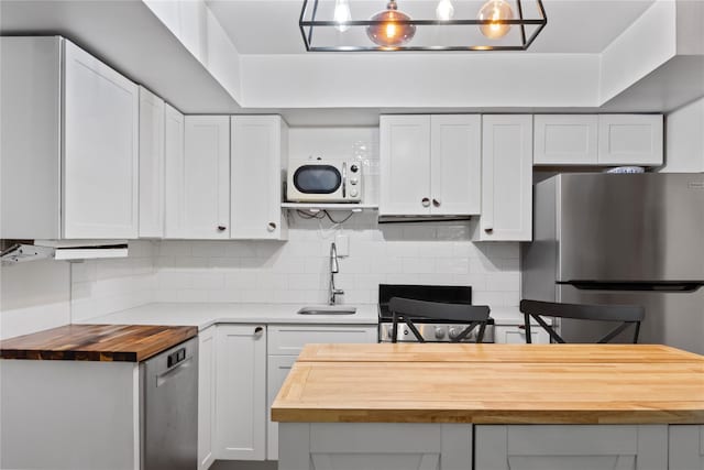 319 Thompson St, Port Jefferson, NY 11777 - kitchen with butcher block counters, a sink, appliances with stainless steel finishes, decorative backsplash, and white cabinetry