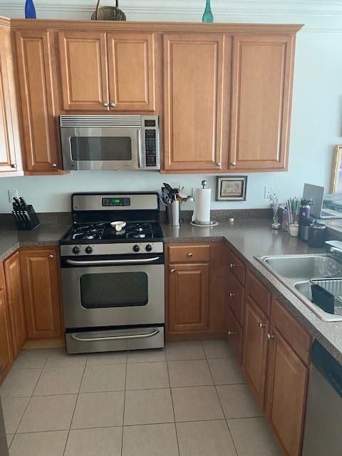 28 Torrey Pine Ln, Bay Shore, NY 11706 - kitchen with stainless steel appliances, a sink, light tile patterned floors, dark countertops, and brown cabinets