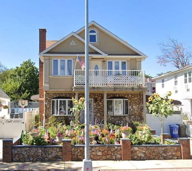 82-44 263rd St, Glen Oaks, NY 11004 - view of front of house with stone siding, a balcony, a chimney, and stucco siding