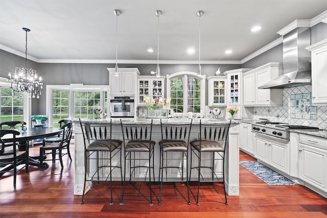 383 Illington Rd, Ossining, NY 10562 - kitchen with stainless steel appliances, wall chimney range hood, light stone countertops, a kitchen breakfast bar, and white cabinets