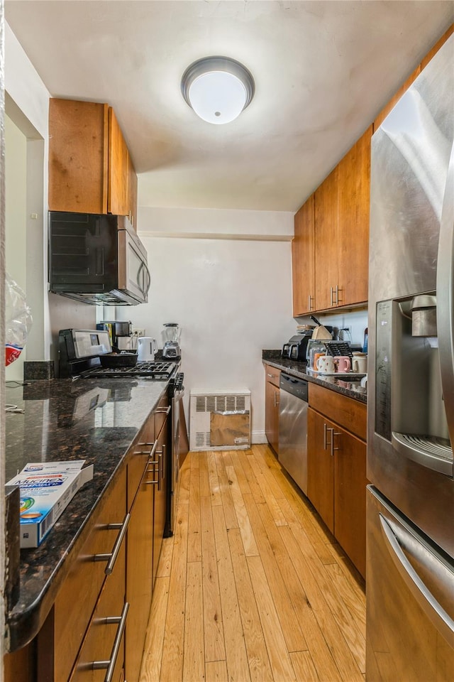 12399 Flatlands Ave Unit 7C, Brooklyn, NY 11207 - kitchen featuring stainless steel appliances, brown cabinetry, light wood-type flooring, and dark stone counters