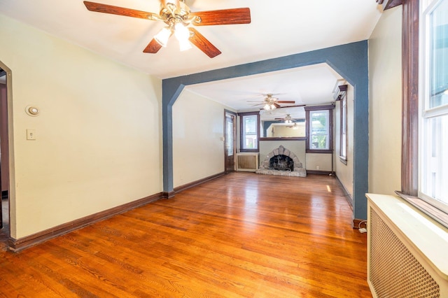 2430 Loft Ave, Baldwin, NY 11510 - unfurnished living room featuring a ceiling fan, arched walkways, light wood finished floors, a fireplace with raised hearth, and radiator heating unit