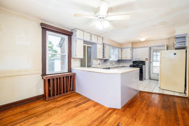 2430 Loft Ave, Baldwin, NY 11510 - kitchen with freestanding refrigerator, black gas range oven, a peninsula, light countertops, and light wood finished floors
