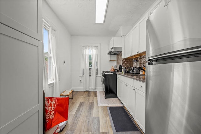 21-38 73rd St, Astoria, NY 11370 - kitchen with freestanding refrigerator, gas range oven, under cabinet range hood, light wood-style flooring, and white cabinetry