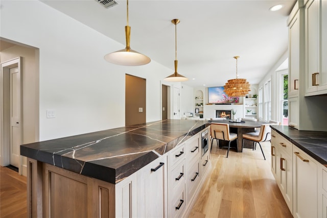 3 Sugar Maple Ct, Dix Hills, NY 11746 - kitchen featuring a warm lit fireplace, dark countertops, open floor plan, light wood-type flooring, and decorative light fixtures
