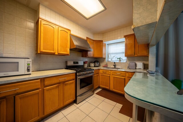 32-23 76th St, East Elmhurst, NY 11370 - kitchen with exhaust hood, stainless steel gas range oven, white microwave, a sink, and light countertops