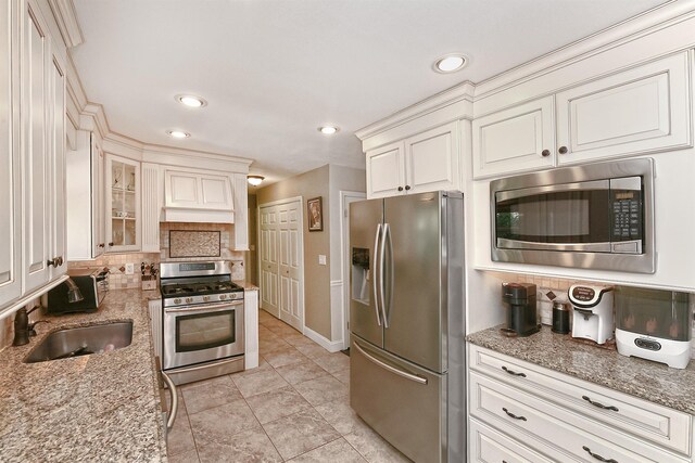 8 Thunder Rd, Miller Place, NY 11764 - kitchen featuring appliances with stainless steel finishes, backsplash, light stone countertops, a sink, and glass insert cabinets
