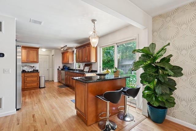 26405 Main Rd, Cutchogue, NY 11935 - kitchen with brown cabinetry, light wood-type flooring, stainless steel appliances, decorative light fixtures, and a kitchen breakfast bar