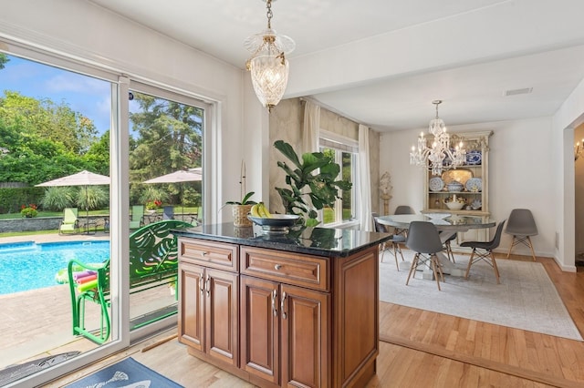 26405 Main Rd, Cutchogue, NY 11935 - kitchen with a chandelier, brown cabinetry, light wood-type flooring, pendant lighting, and dark stone counters