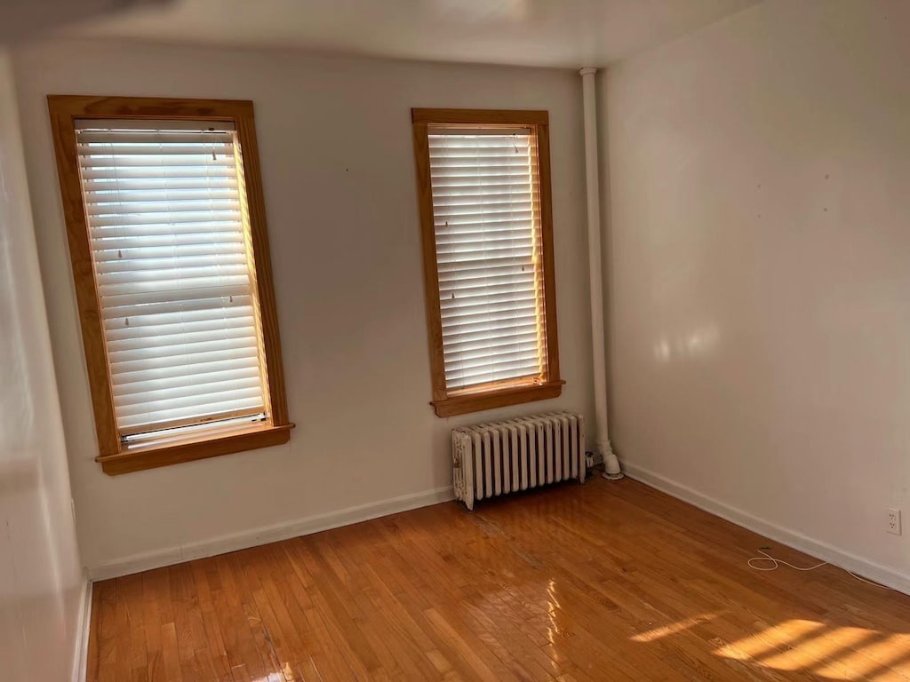 3591 161st St Unit 2J, Flushing, NY 11358 - spare room with radiator, wood-type flooring, and baseboards