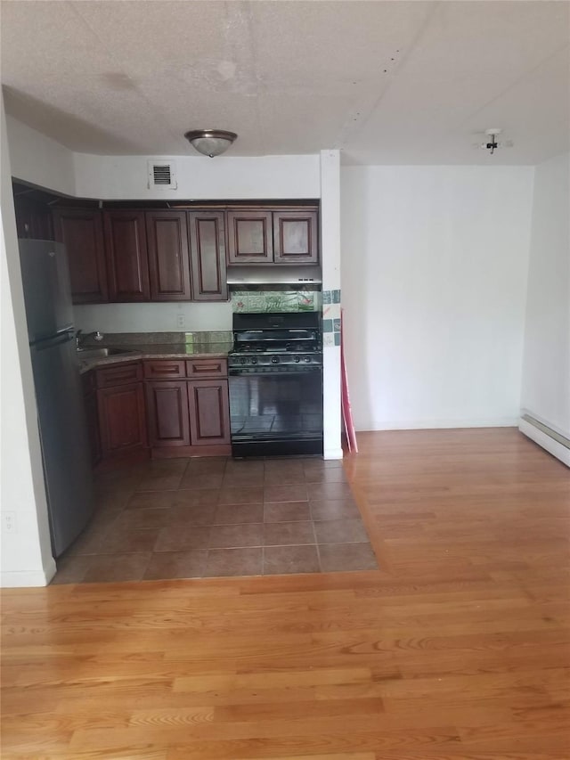 134-46 Maple Ave Unit 1C, Flushing, NY 11355 - kitchen featuring black gas stove, freestanding refrigerator, baseboard heating, light wood-style floors, and under cabinet range hood