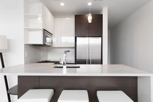 1769 E 13th St Unit 2B, Brooklyn, NY 11229 - kitchen with open shelves, stainless steel appliances, a peninsula, a sink, and white cabinetry