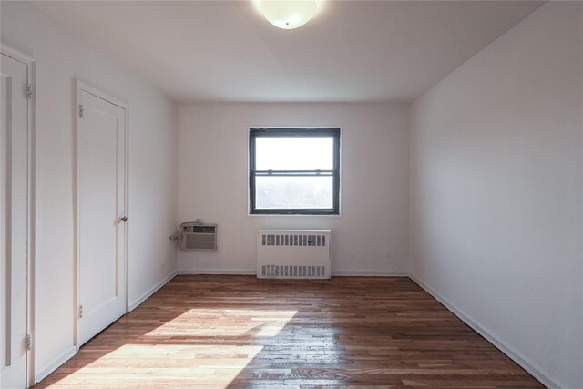 67-09 136th St Unit B, Kew Garden Hills, NY 11367 - unfurnished room with radiator heating unit, wood finished floors, and a wall mounted AC