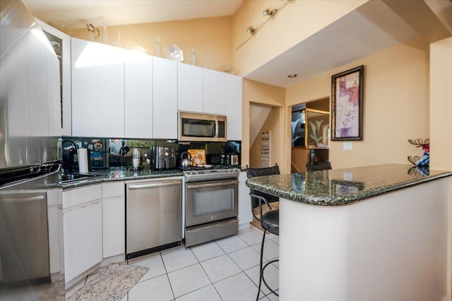22 Cheshire Rd, Inwood, NY 11096 - kitchen featuring stainless steel appliances, white cabinetry, dark stone counters, light tile patterned floors, and a peninsula