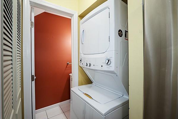 223 Springmeadow Dr Unit E, Holbrook, NY 11741 - laundry area with stacked washer / drying machine, light tile patterned flooring, and baseboards
