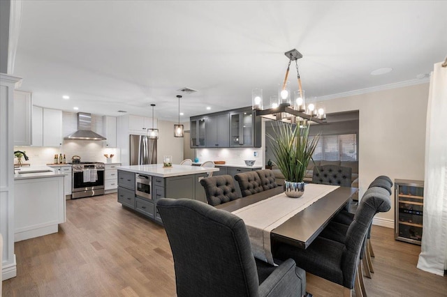 105 Shoreham Way, Merrick, NY 11566 - dining area with beverage cooler, a chandelier, light wood-style flooring, ornamental molding, and recessed lighting