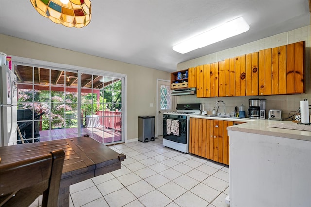 69 Wickham Dr, Warwick, NY 10990 - kitchen with white gas stove, under cabinet range hood, light countertops, a sink, and light tile patterned flooring