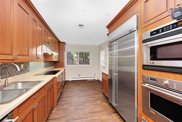 446 Joan Ct, West Hempstead, NY 11552 - kitchen with appliances with stainless steel finishes, a baseboard heating unit, under cabinet range hood, brown cabinets, and dark wood-type flooring