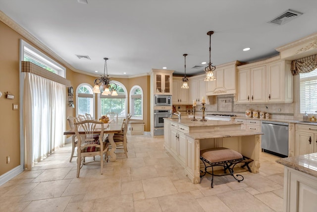 251 Wilmot Dr, Hewlett, NY 11557 - kitchen with appliances with stainless steel finishes, cream cabinets, tasteful backsplash, a center island with sink, and crown molding