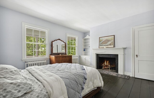 bedroom with radiator, dark wood-style flooring, and a warm lit fireplace