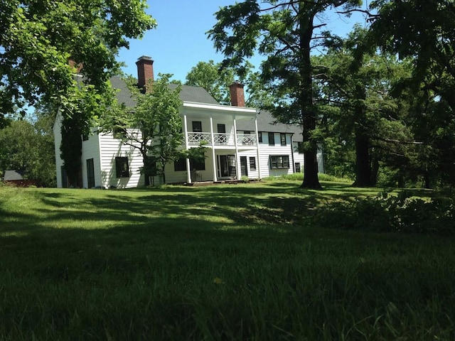back of property featuring a balcony, a lawn, and a chimney