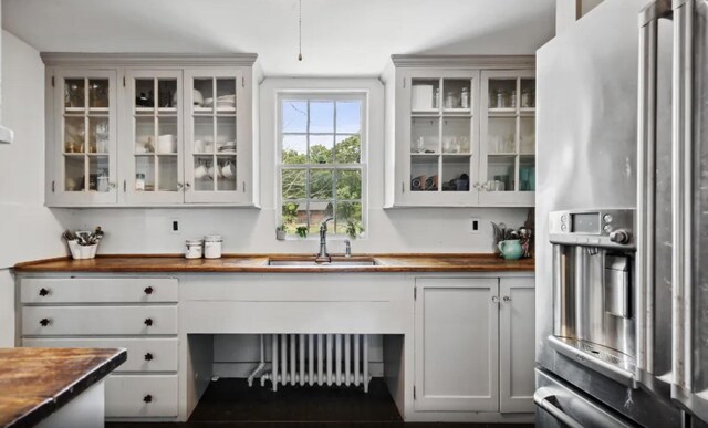 bar featuring stainless steel fridge with ice dispenser, a sink, and radiator heating unit