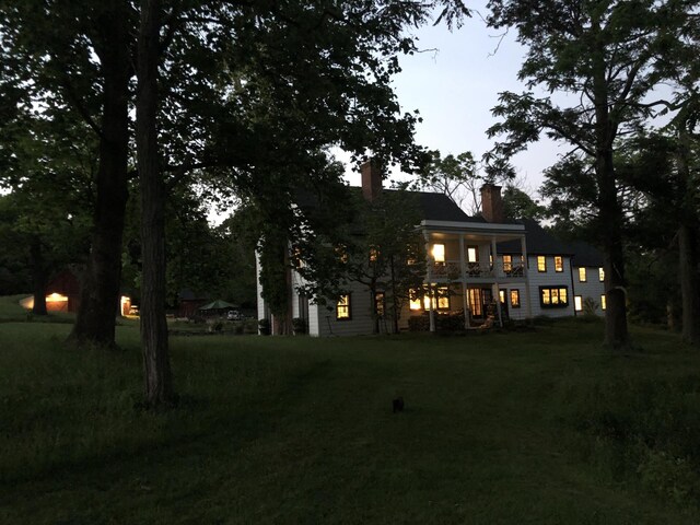 back of property featuring a balcony, a lawn, and a chimney