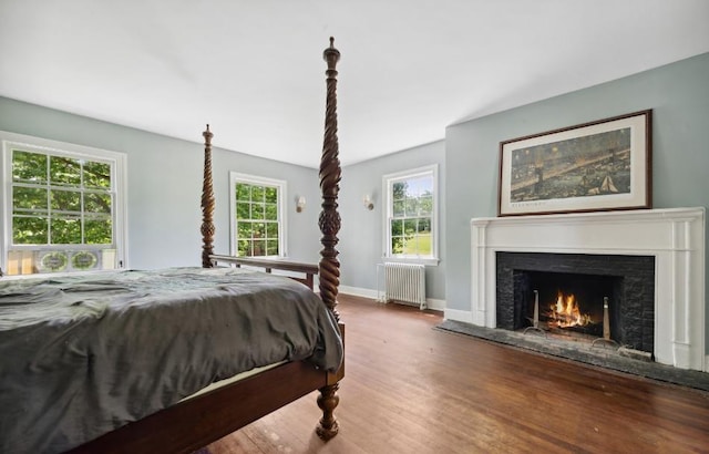 bedroom featuring radiator heating unit, wood finished floors, a lit fireplace, and baseboards