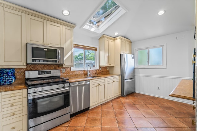 402 Chelsea Ave, West Babylon, NY 11704 - kitchen featuring cream cabinetry, stainless steel appliances, a sink, a skylight, and backsplash