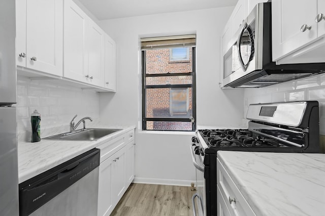 312 Main St Unit 4F, White Plains, NY 10601 - kitchen with stainless steel appliances, backsplash, light wood-style flooring, white cabinetry, and light stone counters