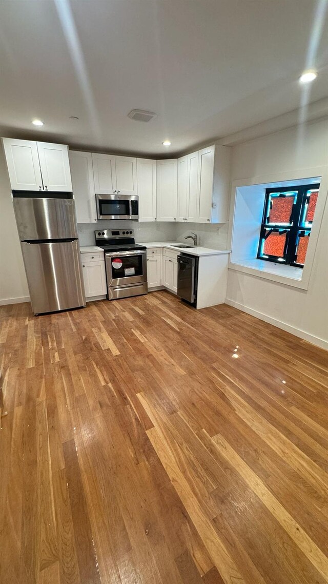 31 Roosevelt Pl, Brooklyn, NY 11233 - kitchen featuring appliances with stainless steel finishes, light wood-style floors, light countertops, white cabinets, and recessed lighting