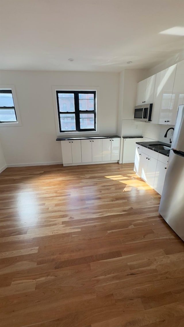 32 Radde Pl, Brooklyn, NY 11233 - kitchen featuring stainless steel microwave, freestanding refrigerator, light wood-style flooring, and white cabinets