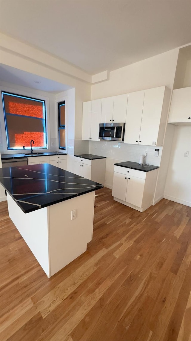 32 Radde Pl, Brooklyn, NY 11233 - kitchen featuring stainless steel microwave, light wood-type flooring, white cabinets, and decorative backsplash