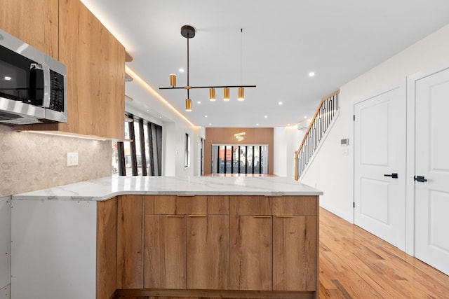 14428 Farmers Blvd, Rochdale, NY 11434 - kitchen with stainless steel microwave, modern cabinets, light wood finished floors, light stone counters, and a peninsula