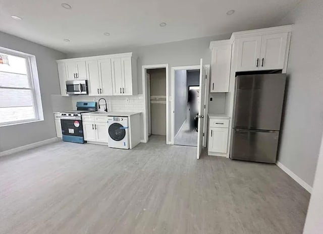 348 Legion St, Brooklyn, NY 11212 - kitchen featuring appliances with stainless steel finishes, washer / clothes dryer, light wood-style flooring, and white cabinetry