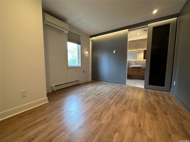 9-01 127th St, College Point, NY 11356 - unfurnished bedroom with baseboard heating, a wall unit AC, light wood-type flooring, and baseboards